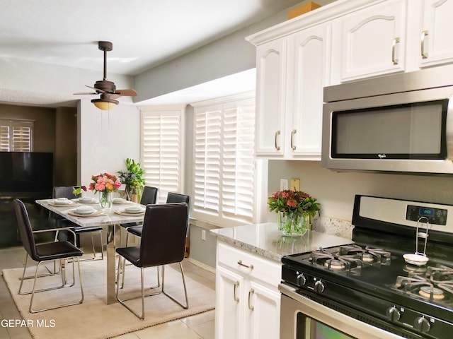 kitchen with light tile patterned flooring, white cabinetry, ceiling fan, stainless steel appliances, and light stone countertops