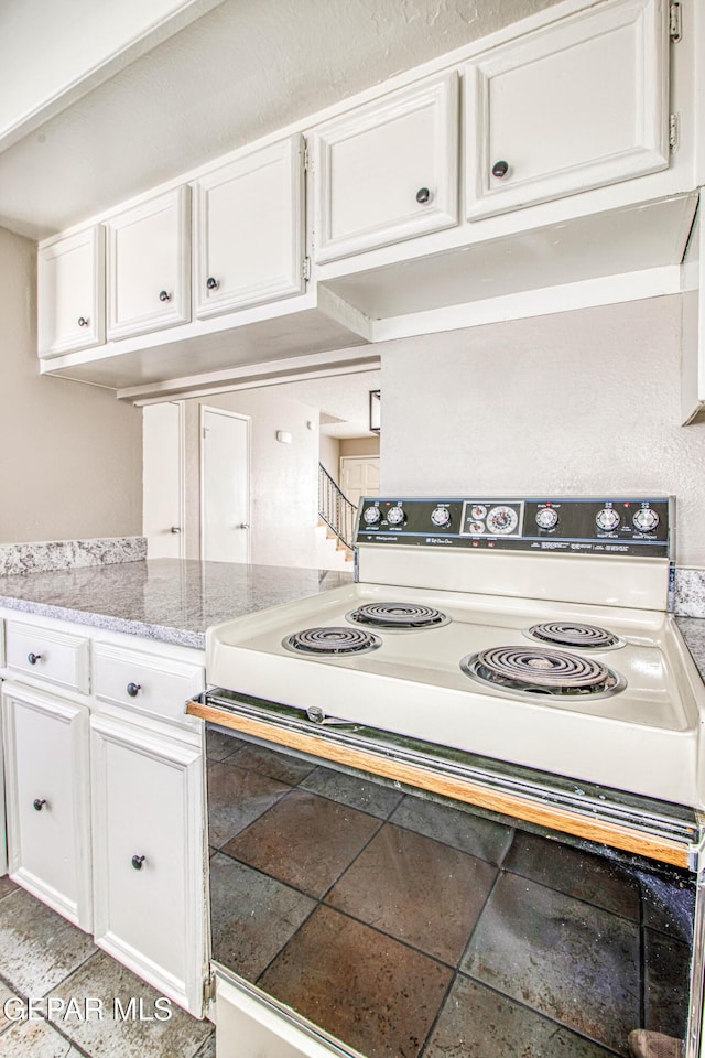 kitchen featuring light stone countertops, electric range oven, and white cabinets