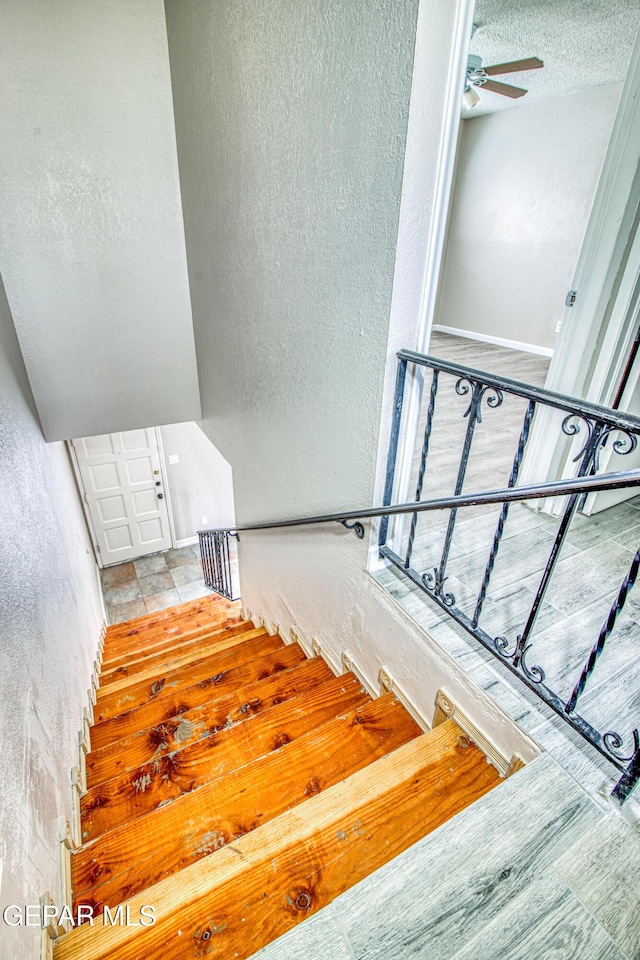 stairs with ceiling fan and a textured ceiling