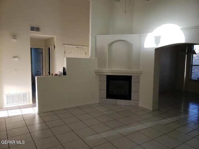 unfurnished living room with a tiled fireplace, a towering ceiling, and visible vents