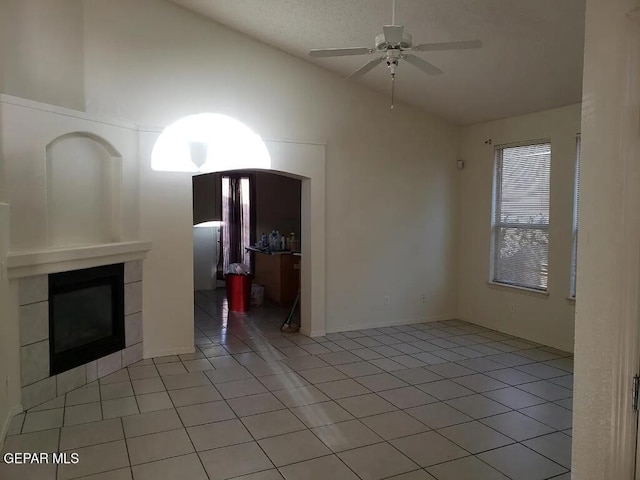 unfurnished living room featuring light tile patterned floors, high vaulted ceiling, a tiled fireplace, and a ceiling fan