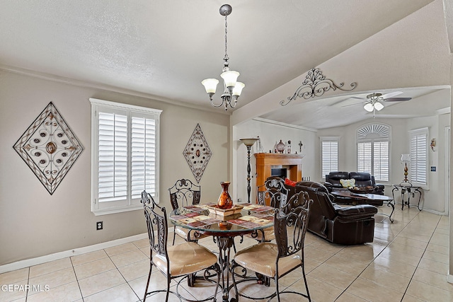 tiled dining space with lofted ceiling, a tiled fireplace, ceiling fan with notable chandelier, and a textured ceiling