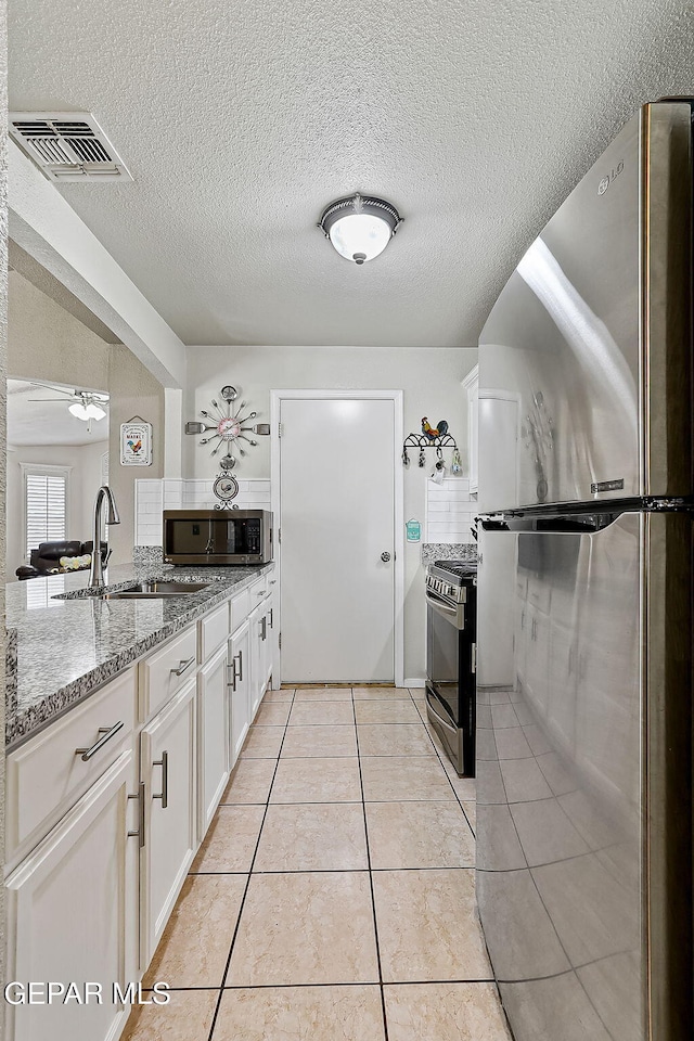 kitchen featuring sink, light stone counters, light tile patterned floors, appliances with stainless steel finishes, and white cabinets