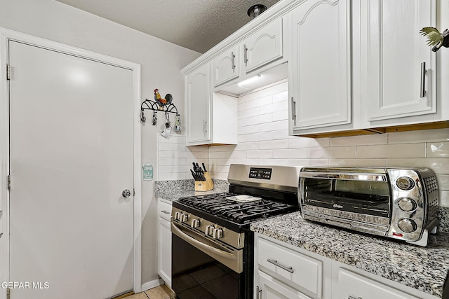 kitchen featuring white cabinetry, decorative backsplash, light tile patterned floors, light stone countertops, and stainless steel range with gas stovetop