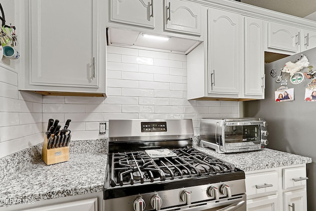 kitchen featuring backsplash, light stone countertops, gas stove, and white cabinets