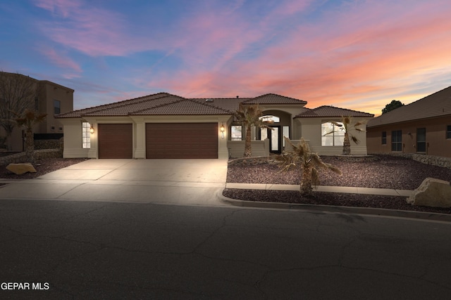 mediterranean / spanish-style house featuring concrete driveway, a tiled roof, a garage, and stucco siding