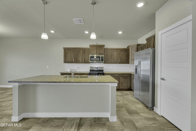 kitchen with appliances with stainless steel finishes, a center island with sink, light stone counters, decorative light fixtures, and sink