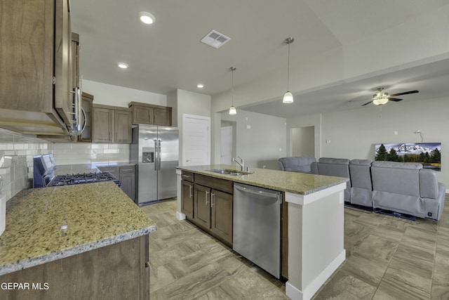 kitchen featuring a center island with sink, appliances with stainless steel finishes, sink, light stone counters, and pendant lighting