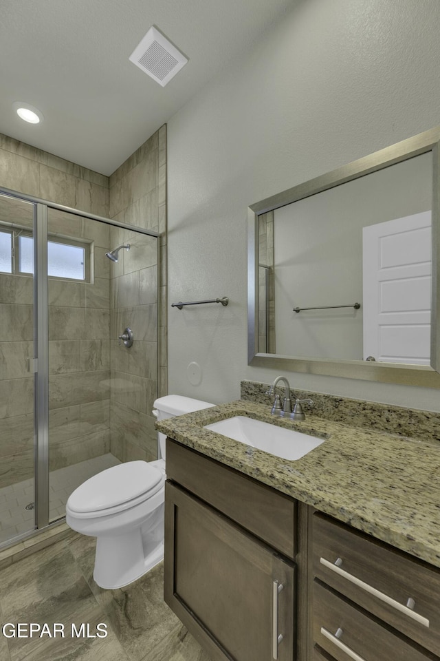 bathroom with toilet, vanity, and a shower with shower door