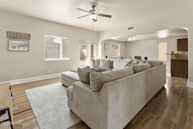 living room with arched walkways, ceiling fan, dark wood-type flooring, visible vents, and baseboards