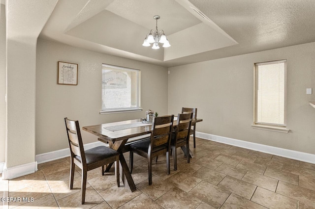 dining area with baseboards, a raised ceiling, and a notable chandelier