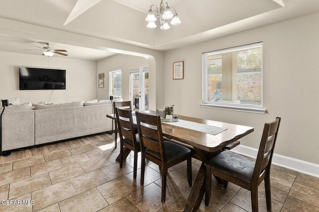 dining area featuring arched walkways, ceiling fan with notable chandelier, a raised ceiling, and baseboards