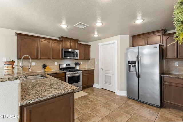 kitchen with visible vents, decorative backsplash, dark stone countertops, stainless steel appliances, and a sink