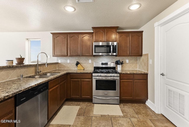 kitchen with stainless steel appliances, a sink, decorative backsplash, and light stone countertops