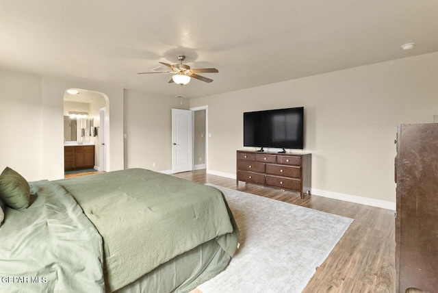 bedroom with baseboards, connected bathroom, arched walkways, and wood finished floors