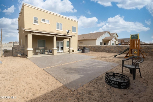 rear view of property with a fire pit, fence, a playground, and stucco siding