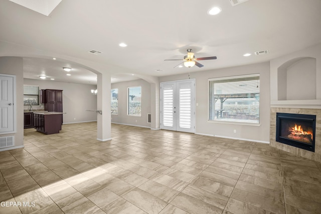 unfurnished living room with a tiled fireplace, ceiling fan, french doors, and light tile patterned floors