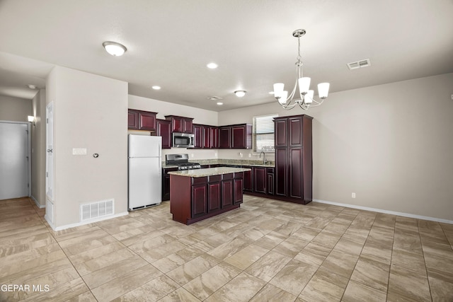 kitchen featuring appliances with stainless steel finishes, light stone counters, pendant lighting, a kitchen island, and an inviting chandelier