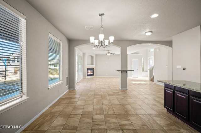 unfurnished dining area with a tile fireplace, ceiling fan with notable chandelier, and a textured ceiling