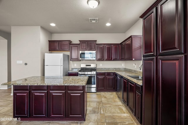 kitchen featuring appliances with stainless steel finishes, sink, a kitchen island, and light stone counters