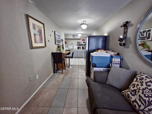 interior space featuring a textured ceiling, a textured wall, light tile patterned flooring, and baseboards