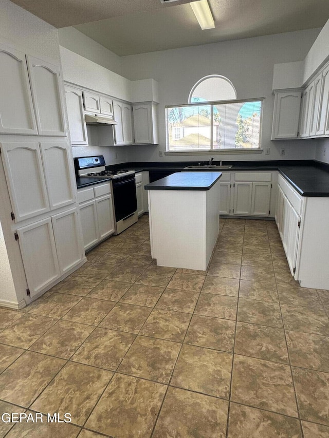 kitchen with tile patterned floors, a kitchen island, range with gas stovetop, sink, and white cabinets