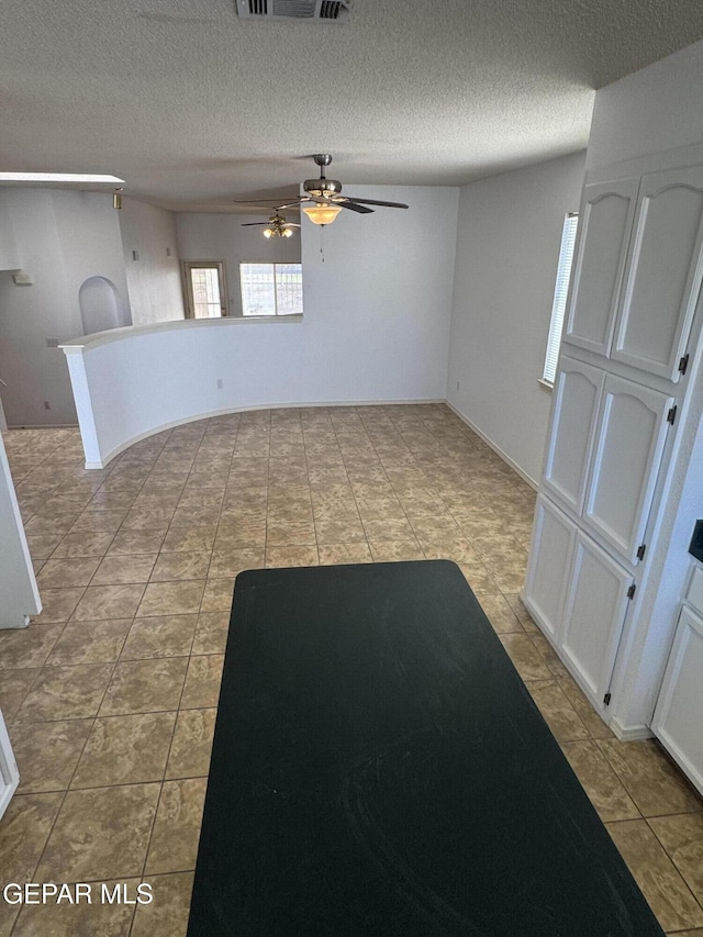 interior space with a textured ceiling, light tile patterned flooring, and ceiling fan