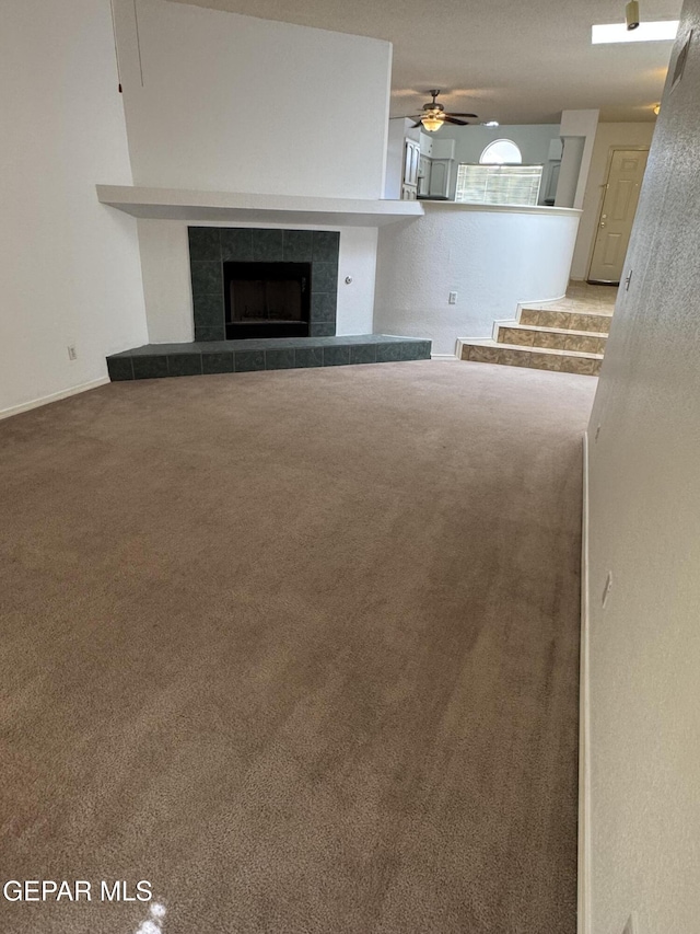 unfurnished living room with a tiled fireplace, carpet flooring, and ceiling fan