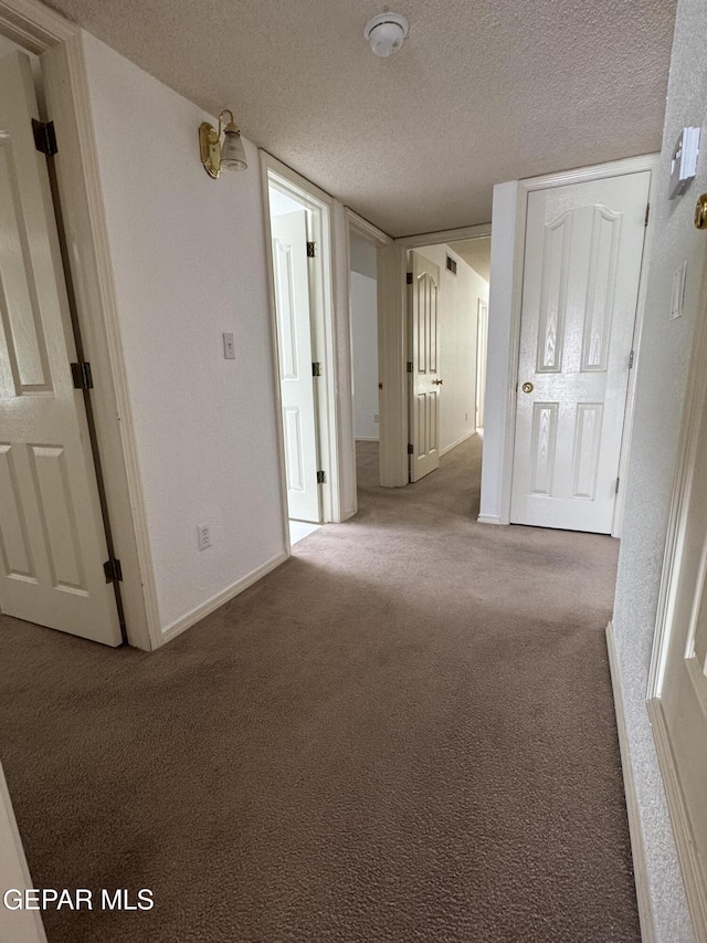 hall with a textured ceiling and light colored carpet