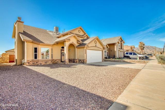 view of front of property featuring a garage, stone siding, driveway, stucco siding, and a chimney