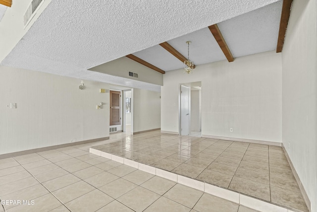 empty room with light tile patterned floors, vaulted ceiling with beams, and a textured ceiling