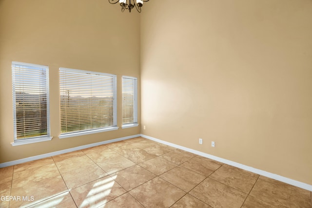 unfurnished room featuring light tile patterned floors, a high ceiling, an inviting chandelier, and baseboards