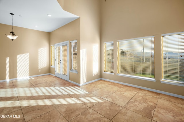 spare room featuring light tile patterned floors, a towering ceiling, and baseboards