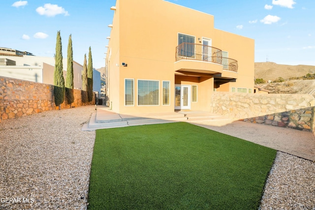 rear view of house with a yard, stucco siding, a patio area, a balcony, and a fenced backyard