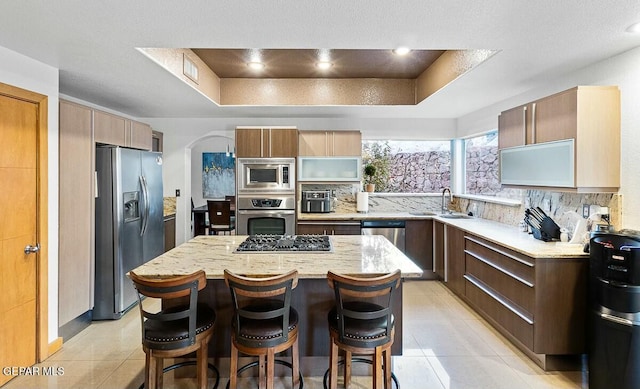 kitchen featuring a tray ceiling, light tile patterned flooring, stainless steel appliances, and a center island