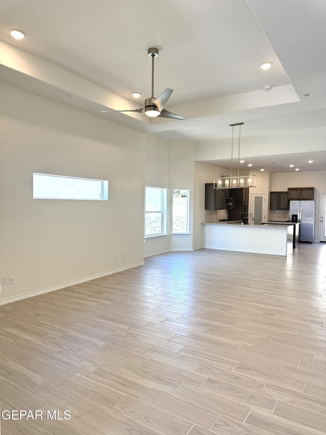 3872 Surmise St, El Paso, TX 79938 - unfurnished living room featuring light wood-type flooring, baseboards, recessed lighting, a ceiling fan, and a tray ceiling