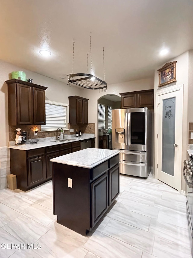 kitchen featuring gas range, a center island, dark brown cabinetry, stainless steel fridge, and sink