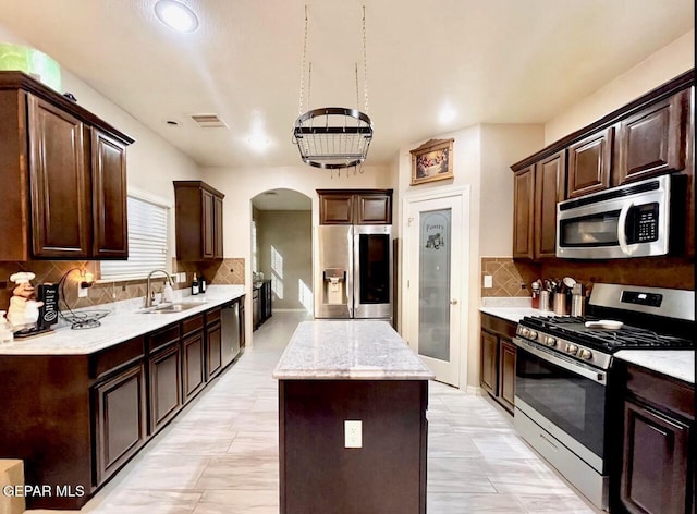 3165 Destiny Point Dr, El Paso, TX 79938 - kitchen with arched walkways, dark brown cabinets, a kitchen island, a sink, and stainless steel appliances