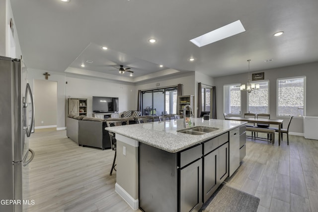 kitchen with sink, pendant lighting, stainless steel fridge, a raised ceiling, and an island with sink