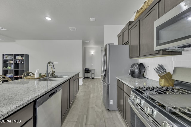 kitchen featuring appliances with stainless steel finishes, light hardwood / wood-style flooring, light stone countertops, backsplash, and sink