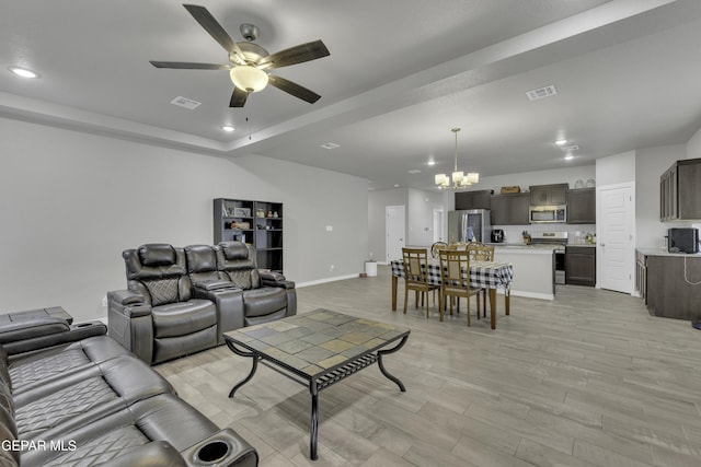 living room with ceiling fan with notable chandelier, light hardwood / wood-style flooring, and a tray ceiling