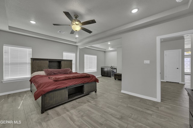 bedroom with ceiling fan, light wood-type flooring, and a raised ceiling