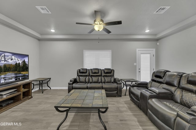 living room with a raised ceiling, light hardwood / wood-style flooring, and ceiling fan