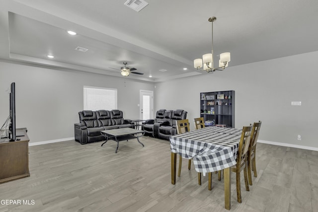 dining room featuring a tray ceiling, ceiling fan with notable chandelier, and light hardwood / wood-style flooring