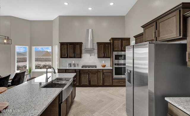 kitchen with stainless steel appliances, light stone countertops, light parquet flooring, wall chimney range hood, and decorative backsplash