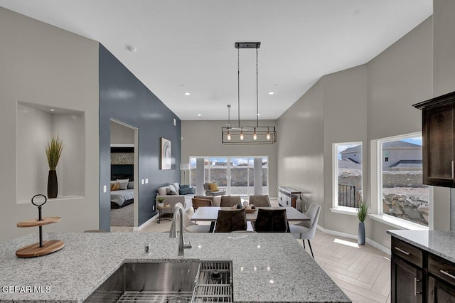 kitchen with a high ceiling, dark brown cabinetry, light stone countertops, sink, and light parquet floors