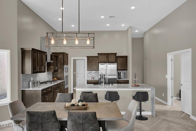 kitchen with a center island with sink, decorative light fixtures, stainless steel appliances, and a towering ceiling