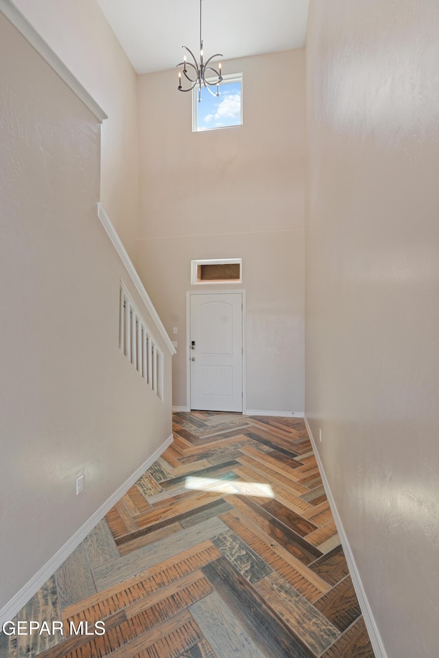 foyer entrance featuring parquet flooring, a high ceiling, and an inviting chandelier