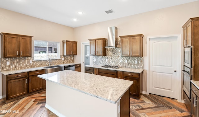 kitchen featuring wall chimney exhaust hood, stainless steel appliances, light stone counters, a center island, and sink