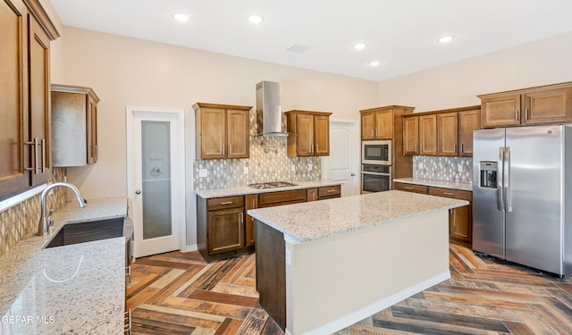 kitchen featuring appliances with stainless steel finishes, wall chimney exhaust hood, light stone countertops, a center island, and sink